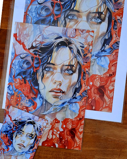 Trois reproductions de l’aquarelle Vulnérable de Julie Vigneron en affiche et carte postale, posées sur une table en bois